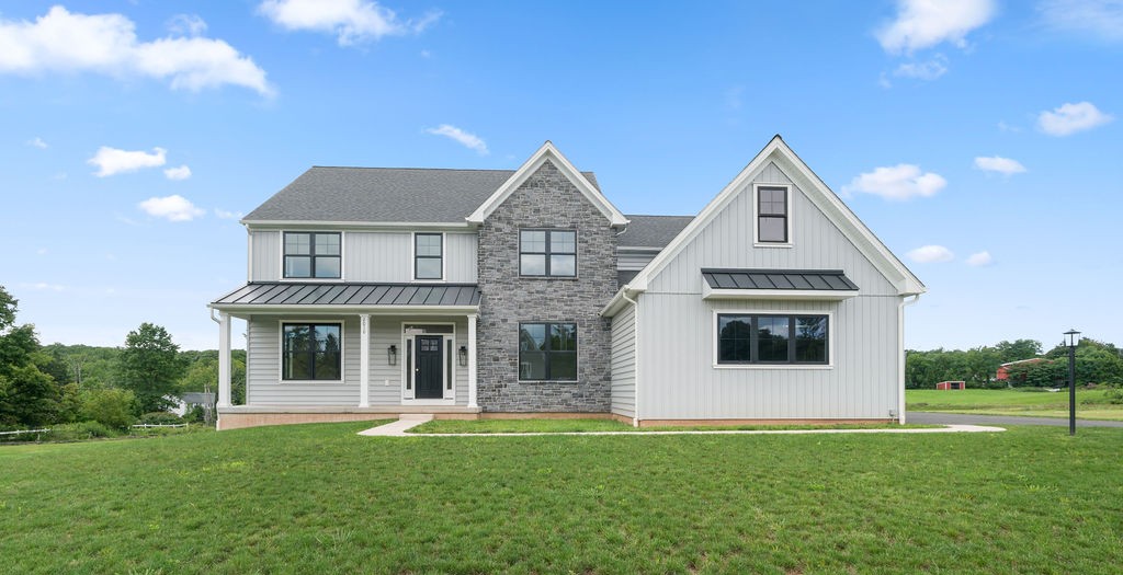Modern two-story house with white siding, gray stone accents, black-framed windows, and a large front lawn under a blue sky with scattered clouds.